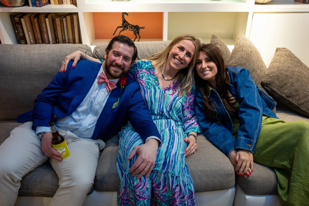 Three adults on a gray sofa posing for a casual photo in a living room with bookshelves behind them.  MitoAction