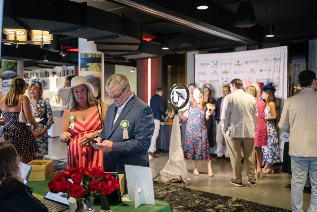 Registration desk at a social event; a man in a suit and a woman in a striped dress examine a program, with red roses in the foreground.  MitoAction