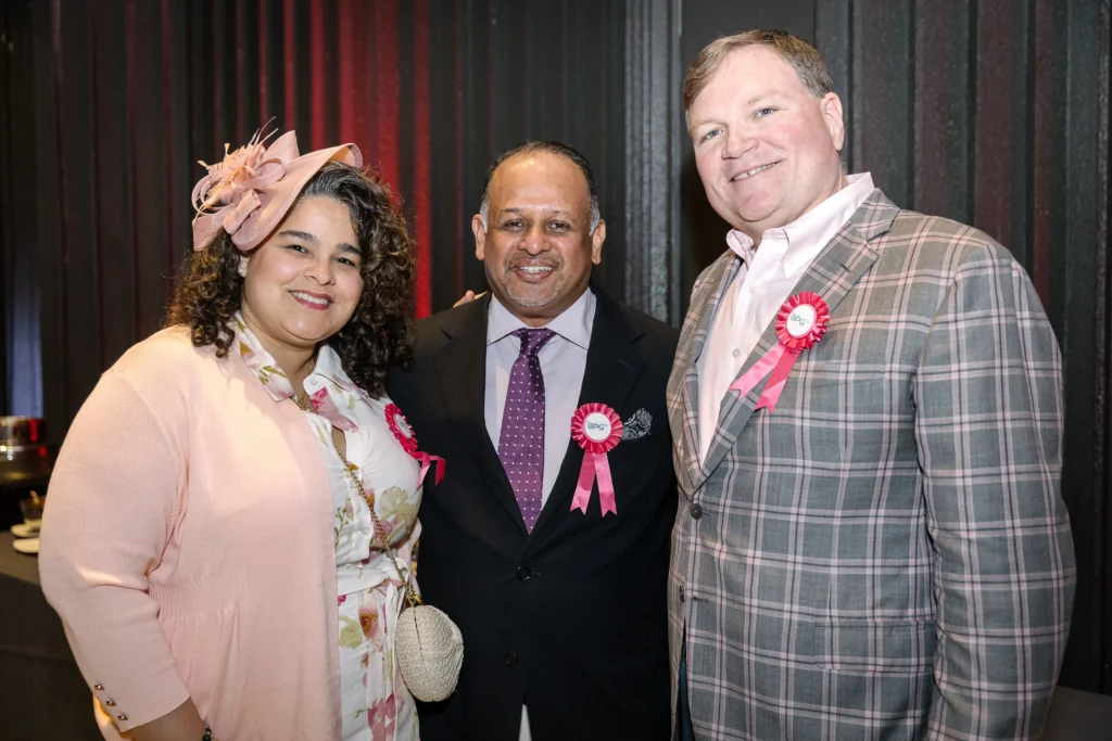 Three people posing for a photo at a formal event, all wearing pink ribbons on their outfits.  MitoAction